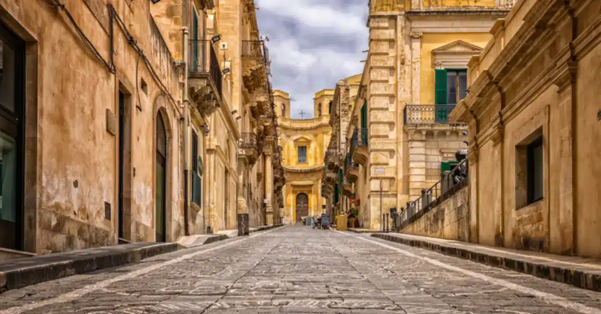 A historic, sunlit baroque street in Noto, Sicily, representing the cultural richness and diverse real estate opportunities available when buying property in southern Italy.
