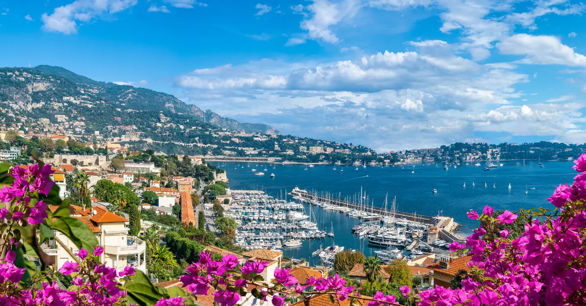 A stunning panoramic view of the French Riviera, a top destination for buying property in france, with a sun-drenched bay, yachts, and hillside homes.